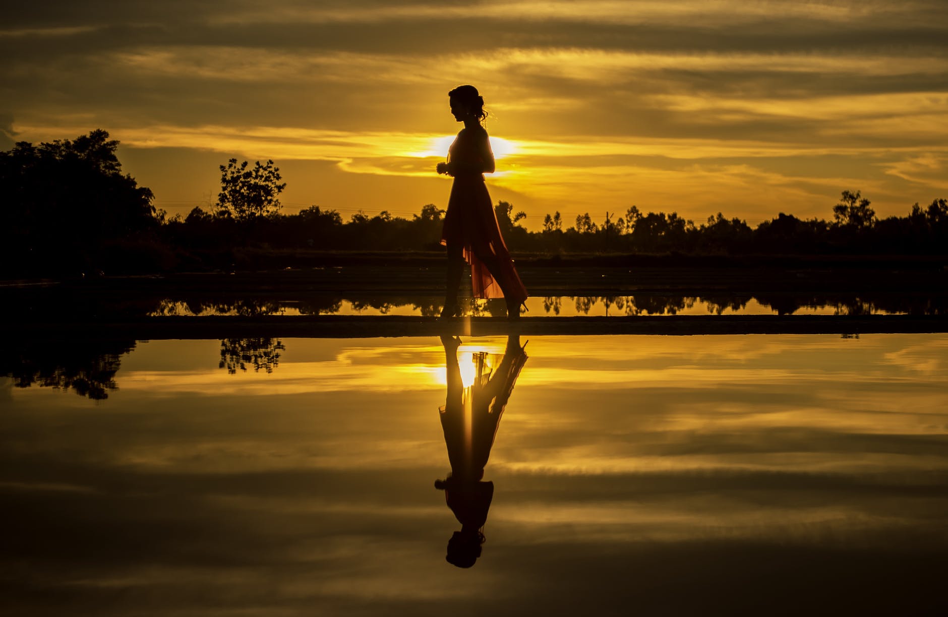 silhouette of man standing on lake at sunset